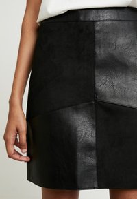 Svart kjol med en blandning av material, inklusive mocka och texturerad läder. Designen är åtsittande med geometrisk paneldetalj.