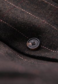 Tissu brun foncé à motifs avec des détails de couture clairs et un bouton rond noir gravé du mot « OMBRE » quatre fois.