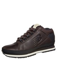 Sneaker in pelle marrone con suola in gomma nera, occhielli metallici e suola intermedia bianca. Presenta un logo impresso sul lato e una coulisse imbottita.