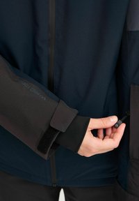 Vodootporna jakna s tamnoplavom tkaninom, džepovima sa patentnim zatvaračem i podesivim manžetama sa čičak trakom. Glatka tekstura i ergonomski dizajn.