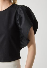 Black top featuring textured puff sleeves made of lightweight fabric. The main body is smooth, with a cropped cut and round neckline.