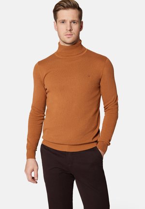 Brązowy sweter typu golf wykonao z miękkiego materiału, z dopasowanym krojem i ściągaczami na rękawach. Ciemne spodnie dopełniają zestaw.