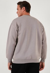Felpa grigia con scollo a girocollo e polsini a costine. Tessuto morbido e testurizzato. Il design presenta una vestibilità comoda, cuciture a vista e nessun ornamento.