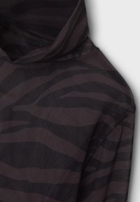 Czarna i ciemnoszara bluza z kapturem w paski zebry, wykonana z lekkiego, teksturowanego materiału, o luźnym kroju i gładkich szwach.