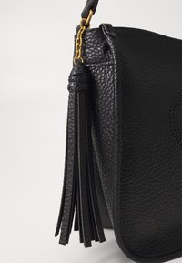 Borsa a tracolla in pelle nera con superficie texturizzata, caratterizzata da un lungo pompon e un dettaglio in catena dorata sulla tracolla.