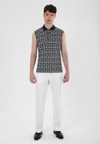 Black and white sleeveless polo shirt featuring a geometric pattern, paired with white trousers, worn with black footwear.