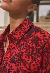 Rode shirt met een zwart luipaardprint, voorzien van een kraag, knoopsluiting en een gladde stofstructuur.