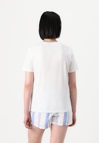 T-shirt branca de algodão com mangas curtas, gola redonda e corte relaxado, combinada com calções listrados em azul claro e branco.