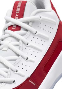 Sneaker atletica bianca e rossa con lacci bianchi, pannelli laterali perforati e striscia rossa con marchio sulla linguetta.