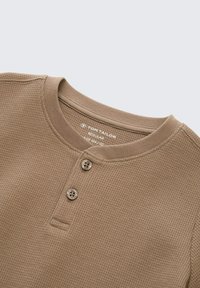 Bruine, gestructureerde lange mouwen henley shirt met een ribbelontwerp. Heeft een ronde halslijn en een knoopsluiting met twee knopen op de borst.