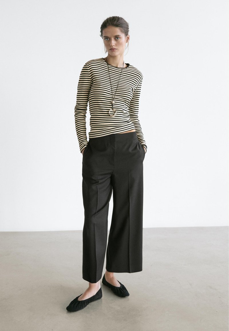Haut à manches longues à rayures noires et blanches assorti à un pantalon noir à taille haute et jambes larges, avec des ballerines noires texturées. Design simple et moderne.