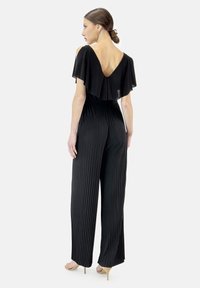 Svart plisserad jumpsuit med djup V-rrygg och fladdermansärmar, tillverkad av lättviktig tyg, med en vid byxor-silhuett.