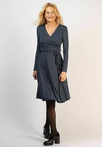 Marinblå omlottklänning med långa ärmar, vitt cirkulärt mönster och A-linjeform. Styla med svarta strumpbyxor och klumpiga klackskor.