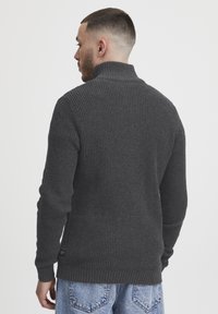 Pulover tricotat de culoare gri închis, cu guler înalt, model texturat și manșete și tiv căptușite. Modelul poartă blugi din denim de culoare bleu deschis.
