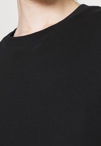 Czarna bawełniana koszulka z okrągłym dekoltem, gładką fakturą i krótkimi rękawami, z minimalnym szyciem i bez widocznych logo ani wzorów.