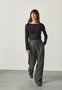 Czarna koronkowa bluzka z długim rękawem w kwiatowy wzór, zestawiona z szarymi szerokimi spodniami plisowanymi. Czółenka ozdobione cyrkoniami dopełniają całość.