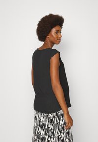 Top preto sem mangas com decote arredondado e um corte descontraído, combinado com uma saia fluida e estampada em preto e branco.
