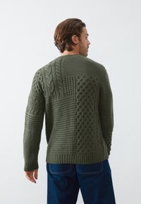 Olivengrøn striktrøje med teksturerede mønstre, herunder kabelstrik og bobler, med en rund halsudskæring og ribbede ærmer.