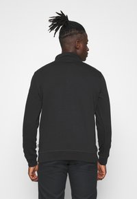Black sweatshirt with a high collar, long sleeves, and ribbed cuffs. Soft texture, simple design, back view showing seams and logo.