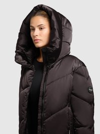 Must täispuhutav jope, millel on suur kapuuts, tõmblukk ja tikitud muster. Vasakul varrukal on logo detail. Sile ja läikiv materjal.