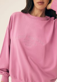 Różowa bluza z okrągłym dekoltem i długimi rękawami, z haftowanym napisem: "West Virginia, EST 2024, STATE OF MIND, BLOOVII."