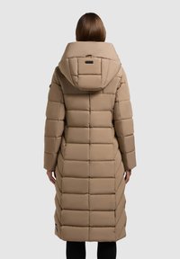 Béžový péřový kabát s velkou kapucí, prošívaným vzorem a délkou po střed lýtek. Má černou štítek u límce a boční zipy.