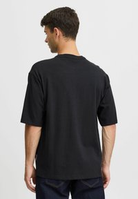 Černé bavlněné tričko s krátkým rukávem, volný střih a kulatým výstřihem. Má jednoduchý design, viditelné švy a žádné grafiky.
