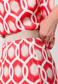 Robe à motifs rouges et blancs avec une texture lisse, des dessins géométriques ronds et une taille élastique beige.