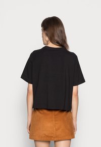 Camiseta negra cortada con mangas cortas, hecha de una tela suave. Combinada con una falda de pana naranja que presenta nervios verticales y un corte recto.