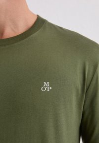 Oliwkowa zielona koszulka z miękkiej bawełny, z okrągłym dekoltem i małym białym logo "M O’P" na piersi. Gładka tekstura, dopasowany krój.