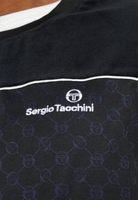 Primo piano di un tessuto nero Sergio Tacchini con logo ricamato bianco e un sottile motivo esagonale in blu scuro.