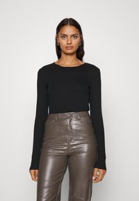 Musthave musta pikaeelsleeve'i topp, millel on ümmargune kaelus, on koos läikivate pruunide kunstnahast kõrge vöökoha pükstega, millel on tekstuuriga muster.