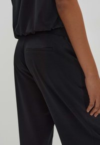 Zwarte broek van gladde stof met een slim fit, zijzak en een subtiele achterkant zakdetail. Eenvoudig en veelzijdig ontwerp.