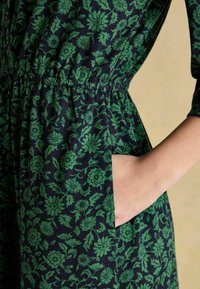 Tumesinine kleit rohelise lillemustriga, elastne vöökohaga ja küljetaskuga, millel on kerge kangas ja kolmandikvarrukad.