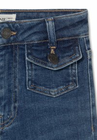 Los jeans de denim azul oscuro presentan un diseño clásico de cinco bolsillos, con costuras naranjas en contraste y acentos de botón metálico.