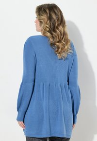 Helles blaues langärmliges Sweatshirt mit geripptem Textur, Peplum-Design und schmalen Bündchen. Die Rückansicht zeigt sanfte Drapierung und eine lockere Passform.