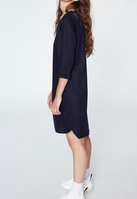 Navyblå klänning med avslappnad passform, trekvartslånga ärmar, sidokilar och en enkel design, bärs med vita sneakers och ankelsockor.