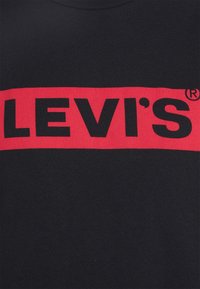 Černé bavlněné tričko s výrazným červeným horizontálním pruhem s nápisem "LEVI'S" velkými černými písmeny. Kulatý výstřih, krátké rukávy.