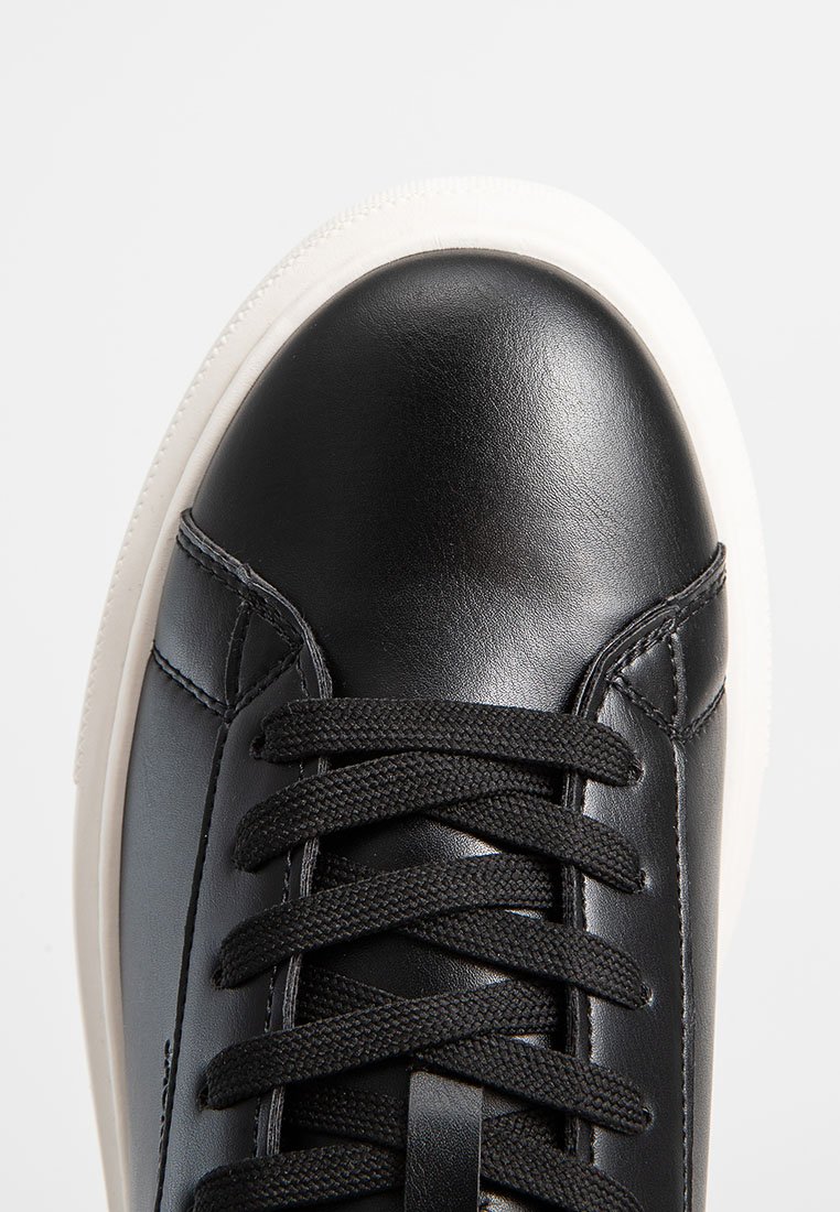 Zapatilla negra de cuero con puntera redonda, cordones negros y suela de goma blanca. Diseño elegante que presenta sutiles detalles de costura.