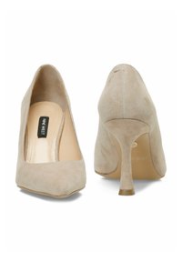 Béžové semišové lodičky s čtveratou špičkou a štíhlým, špičatým podpatkem. Interiér ukazuje béžovou stélku s nápisem "NINE WEST." Hladký povrch.