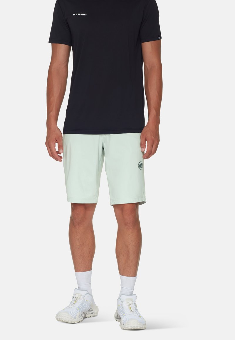 Svart kortärmad t-shirt med vitt logotyp, parat med ljus mintgröna shorts med sidofickor och en logotyp. Vita sneakers och strumpor ingår.