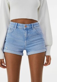 Ljust blå denimshorts med uppvikta muddar, med en femfickorsdesign och lätt nött detaljering. Knappar och sömmar är i kontrasterande färg.