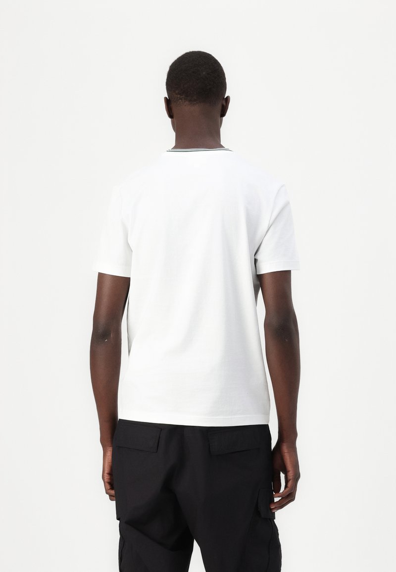 T-shirt en coton blanc avec un col rond, des manches courtes et un ourlet plat. Le dos présente un design épuré et minimal sans aucune graphique.