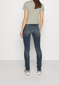 Dunkelblaue, schmale Jeans mit einem verwaschenen Effekt, kombiniert mit einem hellgrünen, cropped T-Shirt. Hat Gesäßtaschen und einen mittelhohen Bund.