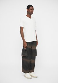 Biela tričko s v-neck výstrihom skombinované s voľnými čiernymi cargo nohavicami s hnedými pruhmi a viacerými vreckami. Nosené s bielymi teniskami.