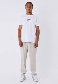 Witte T-shirt met korte mouwen en zwart logo, gecombineerd met lichtgrijze, losse broek. Sneakers met een gestructureerde zool maken de outfit compleet.