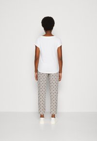 Valkoinen lyhythihainen paita yhdistettynä kuvioituihin vaaleanharmaisiin housuihin, joissa on punaisia ja sinisiä geometrisia kuvioita, käytetty valkoisten lenkkarien kanssa.