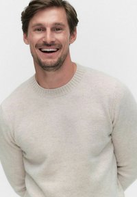 Ljusgrå stickad tröja med ribbad rund halsringning, tillverkad av mjukt tyg, åtsittande vid axlarna, med subtil textur.