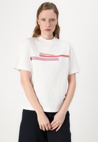 Bijela pamučna majica s okruglim izrezom i kratkim rukavima, s crvenim i roza horizontalnim prugama i natpisom "Karl Lagerfeld" na prednjem dijelu.