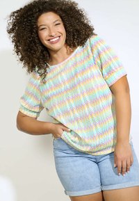 Top a maniche corte con un motivo zigzag multicolore in tonalità pastello, abbinato a pantaloni corti in denim con risvolti.